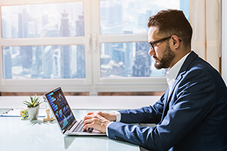 Business man in a suit at a desk using a business intelligence platform to analyze data on his laptop.