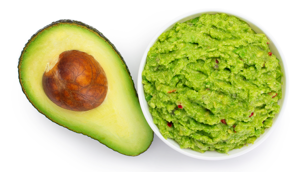 Schüssel mit frischer Guacamole neben einer halben Avocado mit Stein.