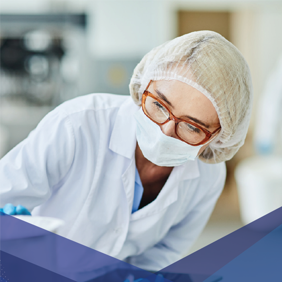 Labortechniker mit Maske, Kopfbedeckung und Brille, der in einer klinischen oder sterilen Umgebung arbeitet.