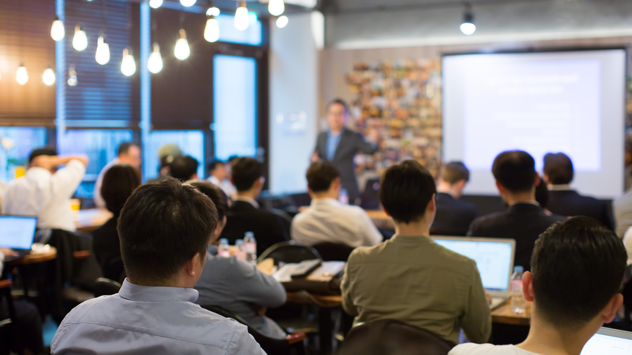 Audience Listens to Lecturer at a Conference Meeting Seminar Training. Group of People Hear Presenter Give Speech . Corporate Manager Speaker Gives Business Technology and Economic Forecast.