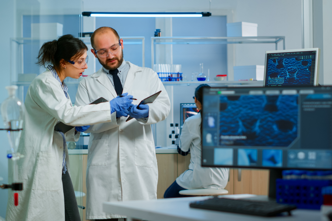 Modernes Labor für die medizinische Forschung: Zwei Wissenschaftler bei der Arbeit, mit Tablet, bei der Analyse von Tests, im Gespräch. Fortschrittliches wissenschaftliches Pharmalabor für die Entwicklung von Medikamenten und Biotechnologie.