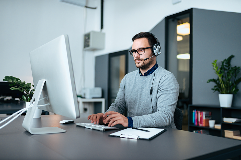 Young male IT specialist wearing a headset working with infrastructure analytics on a computer.