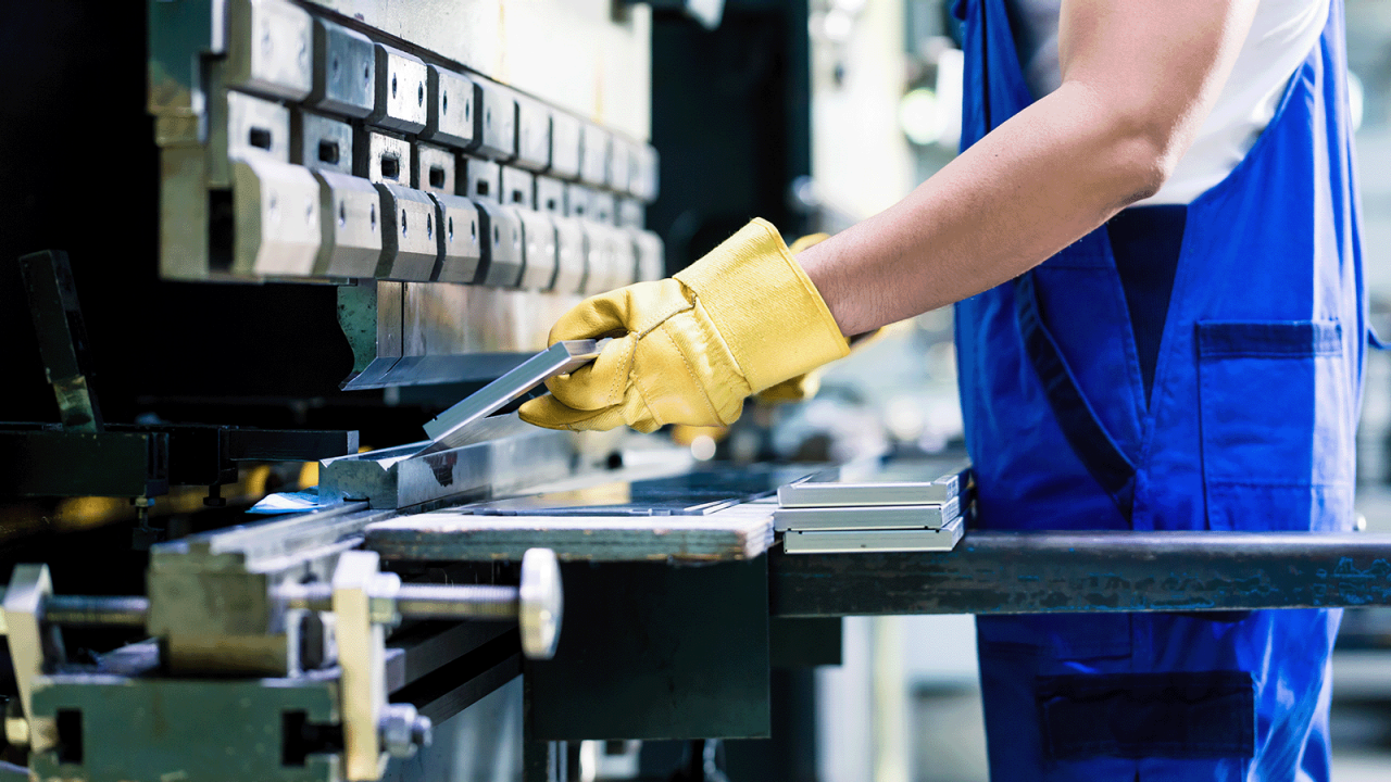 Trabalhador industrial inspecionando uma bancada de peças de trabalho no piso da fábrica.